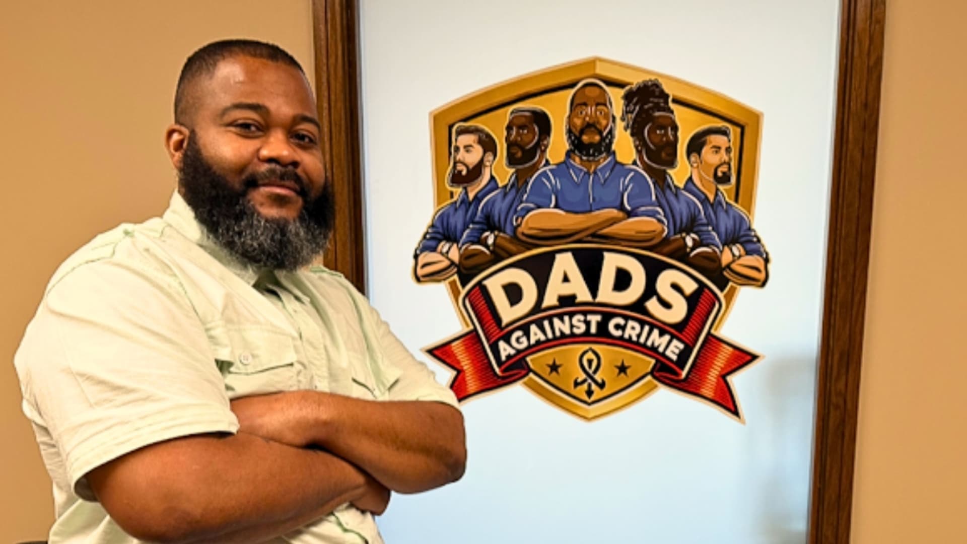 Andre Harris, founder of Dads Against Crime stands smiling by the logo