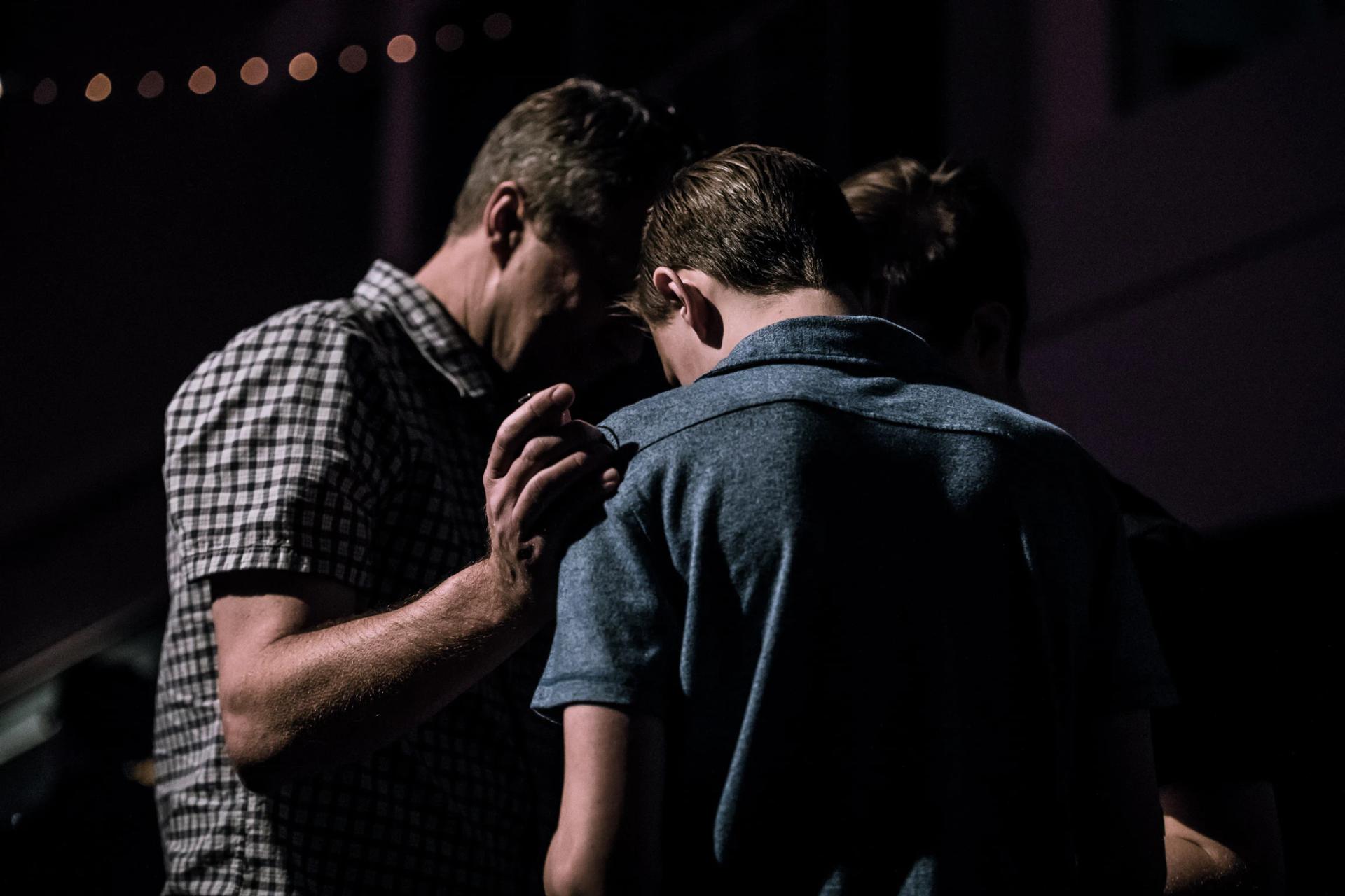 two men with heads bowed together praying