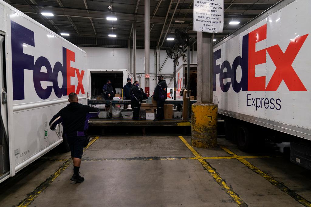  FedEx delivery trucks parked next to conveyor belt while being loaded with packages for delivery