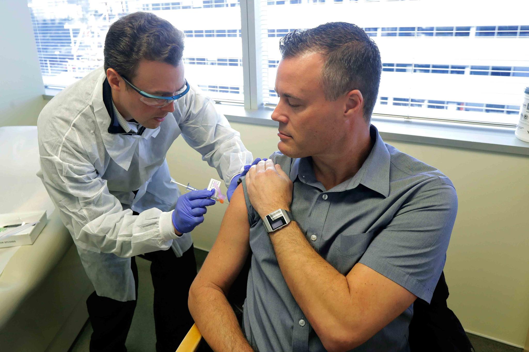 Pharmacist Michael Witte, left, gives Neal Browning, right, a shot in the first-stage safety study clinical trial of a potential vaccine for COVID-19
