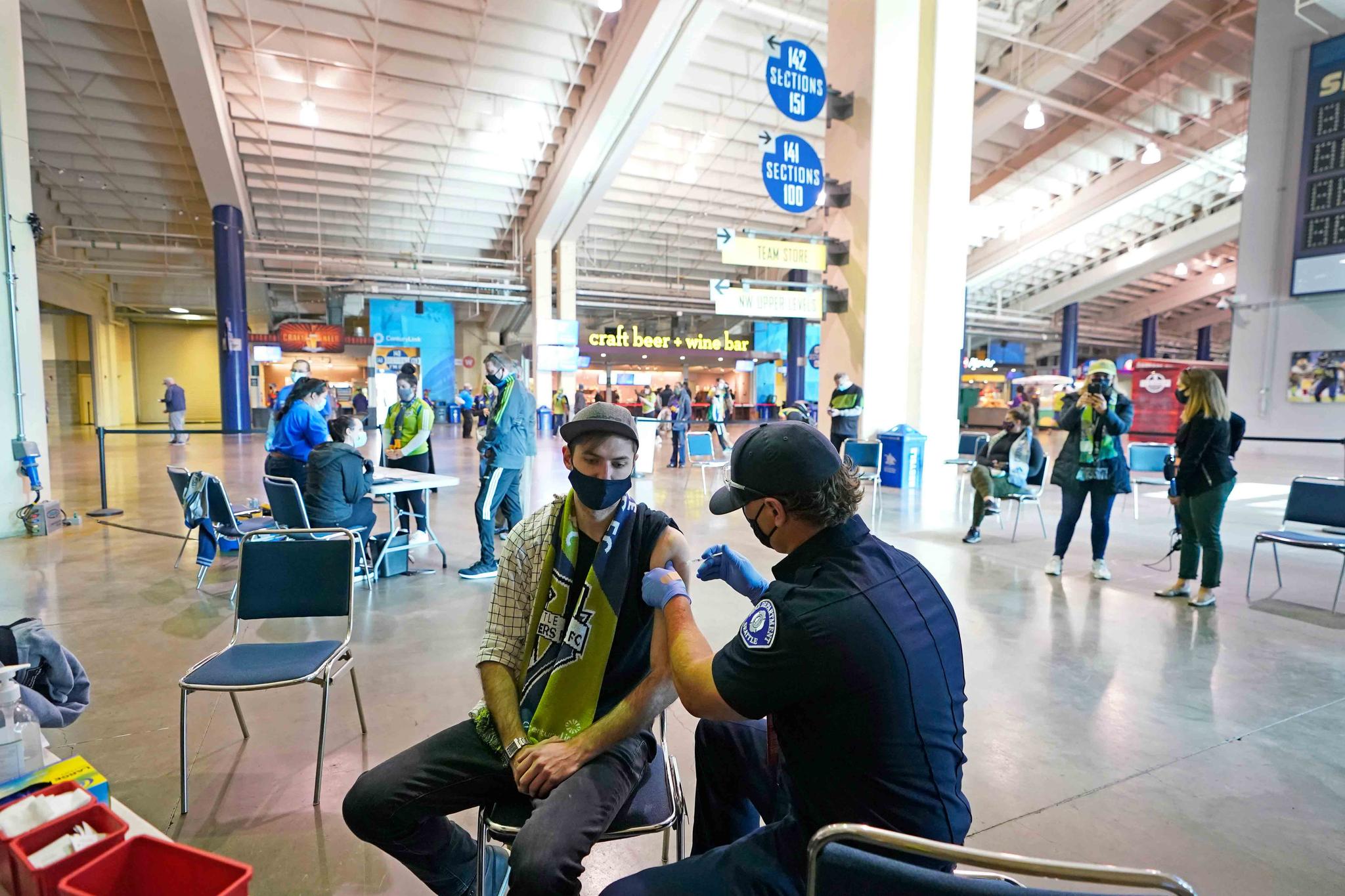 Austin Kennedy, left, a Seattle Sounders season ticket holder, gets the Johnson & Johnson COVID-19 vaccine at a clinic in a concourse at Lumen Field prior to an MLS soccer match between the Sounders and the Los Angeles Galaxy.